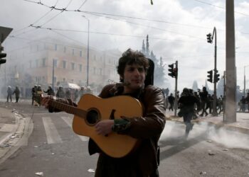 Διαδηλωτής παίζει κιθάρα και τραγουδά την ώρα που δίπλα του πέφτουν μολότοφ και πέτρες