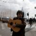 Διαδηλωτής παίζει κιθάρα και τραγουδά την ώρα που δίπλα του πέφτουν μολότοφ και πέτρες